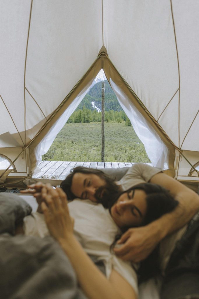 Couple relaxing in a tent with a beautiful mountain view, symbolizing outdoor romance and adventure.
