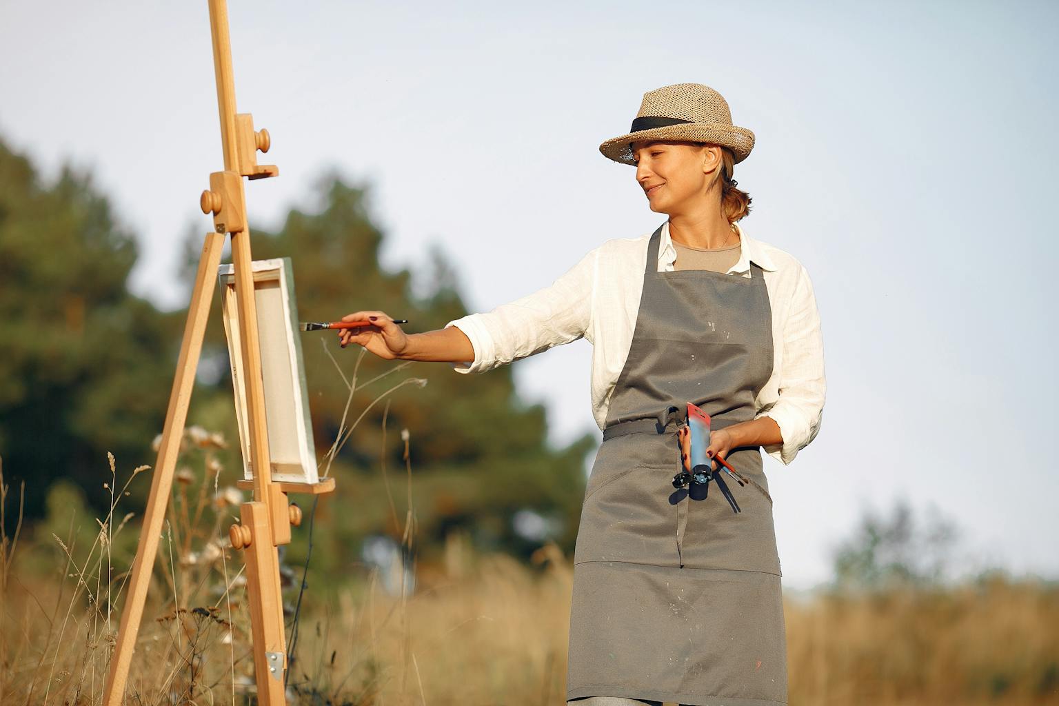 A woman artist painting on a canvas outdoors, enjoying a peaceful and creative moment amidst nature.