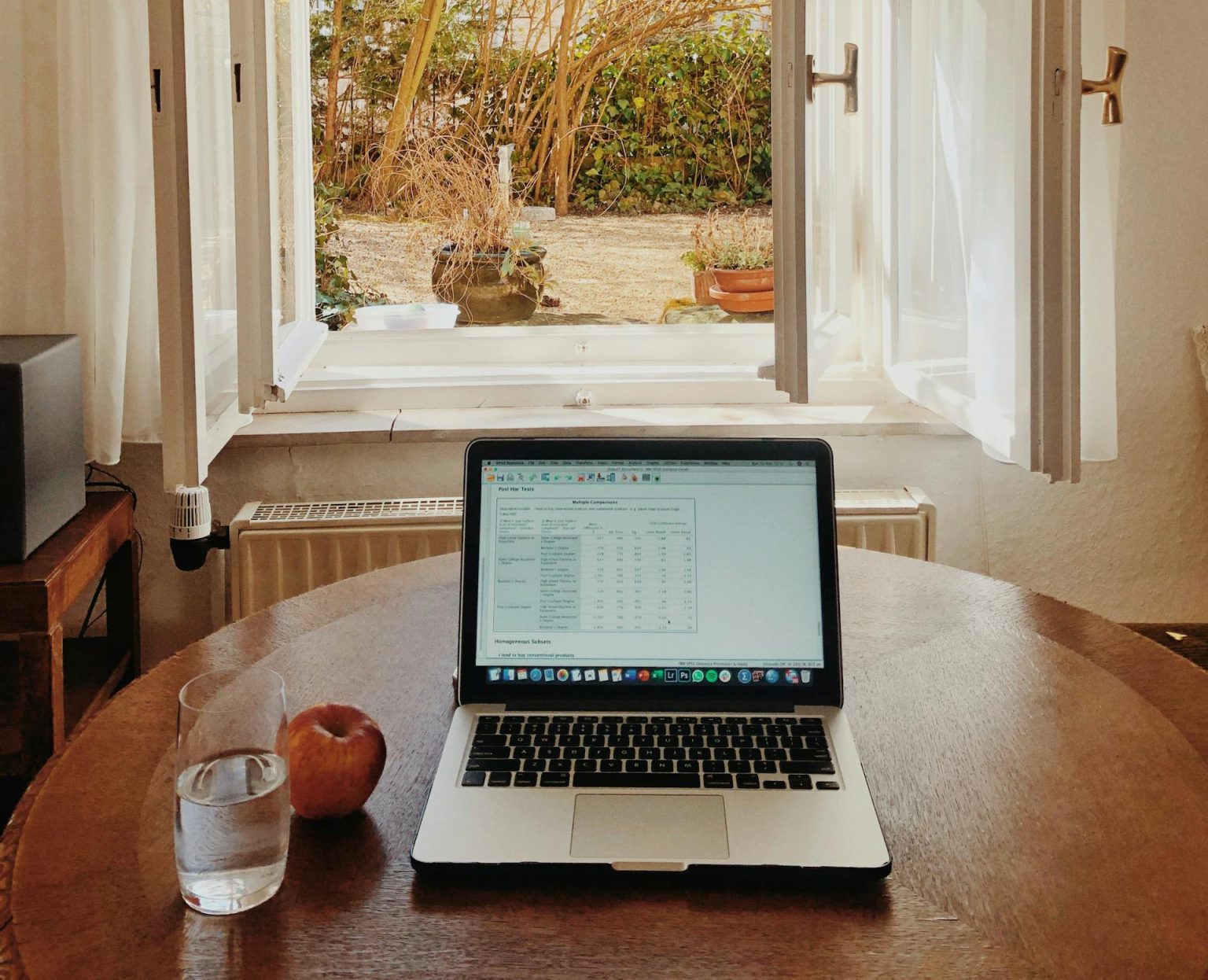 Cozy home office setup with laptop on desk facing an open window offering a view of a garden.
