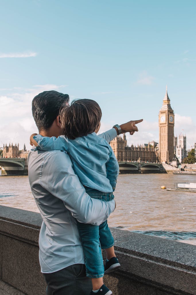 Father holds child as they point towards Big Ben on a sunny day in London.