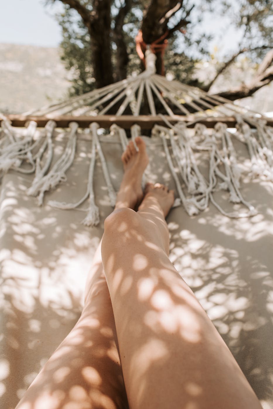 A serene view of a person's legs in a hammock under dappled sunlight, perfect for relaxation.
